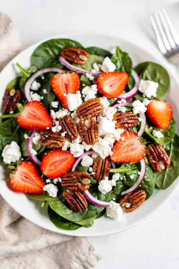 Fresh strawberry spinach salad with candied pecans and feta cheese in a bowl.