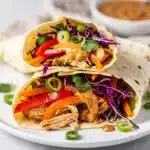 Thai peanut chicken wraps with fresh vegetables and creamy sauce on wood table