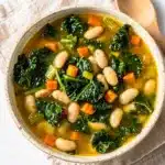 Creamy white bean kale soup recipe in a rustic ceramic bowl.