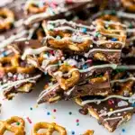 Chocolate covered pretzel bark with sprinkles and salt on rustic board