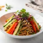 Cold sesame noodle salad with creamy peanut dressing and fresh vegetable toppings.