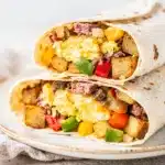 Corned beef hash breakfast burrito with eggs cheese and potatoes on rustic board