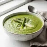 Creamy green asparagus soup garnished with tips and Parmesan cheese