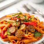 Creamy Cajun sausage pasta with penne and bell peppers in a white bowl.