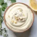 Creamy garlic aioli in a bowl with minced garlic, lemon, and fresh thyme.