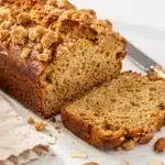 Moist banana bread slice with cinnamon almond crumble topping on rustic board.