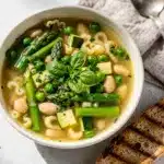 Rustic bowl of spring minestrone soup with asparagus, peas, and pasta.