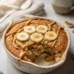 Baked peanut butter banana overnight oats with honey and cinnamon in ramekin.