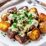 Cheesy garlic butter steak bites and crispy potatoes on a white pan.