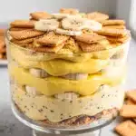 Classic Banana Pudding in a glass trifle bowl shows layered wafers and creamy custard.