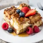 Classic overnight French toast bake with berries and maple syrup on rustic table.