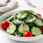 Creamy cucumber dill salad with fresh tomatoes in a bright white bowl.