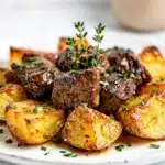 Homestyle garlic butter steak bites and crispy potatoes on a rustic wooden board.