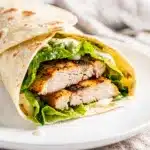 Grilled chicken Caesar wrap sliced open on a rustic wooden board.