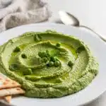Creamy spring pea and mint hummus garnished with peas and olive oil.