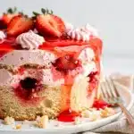 Creamy strawberry jello poke cake slice with fresh strawberries and whipped cream