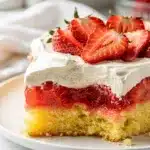 Old Fashioned strawberry jello poke cake slice with whipped cream and fresh strawberries.