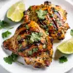 Cilantro lime grilled chicken thighs with charred marks and fresh lime wedges.