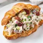 Creamy chicken salad croissant sandwich with celery and cranberries on white plate
