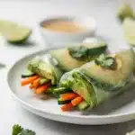 Fresh cucumber avocado summer roll with peanut sauce on a white plate.