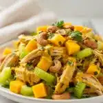 Curried chicken salad with mango in a white bowl, featuring vibrant yellow dressing.