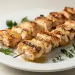Golden brown garlic parmesan grilled chicken skewers on a rustic wooden board.
