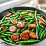 Glossy honey garlic sausage and green beans in cast iron.
