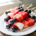 Patriotic watermelon fruit skewers with strawberries and blueberries on a rustic board