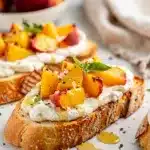 Rustic peach bruschetta with whipped ricotta on a dark slate board.