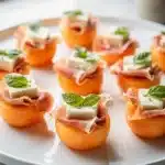 Prosciutto melon bites with creamy mozzarella on a rustic wooden board.