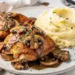 Crispy smothered chicken thighs in creamy mushroom gravy on rustic plate.