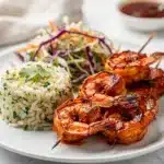 Spicy BBQ shrimp skewers with glossy sauce on a wooden board