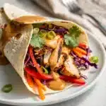 Spicy Thai peanut chicken wrap with colorful vegetables and creamy peanut sauce