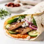 Grilled chicken wrap with sun dried tomato spread on rustic wooden board
